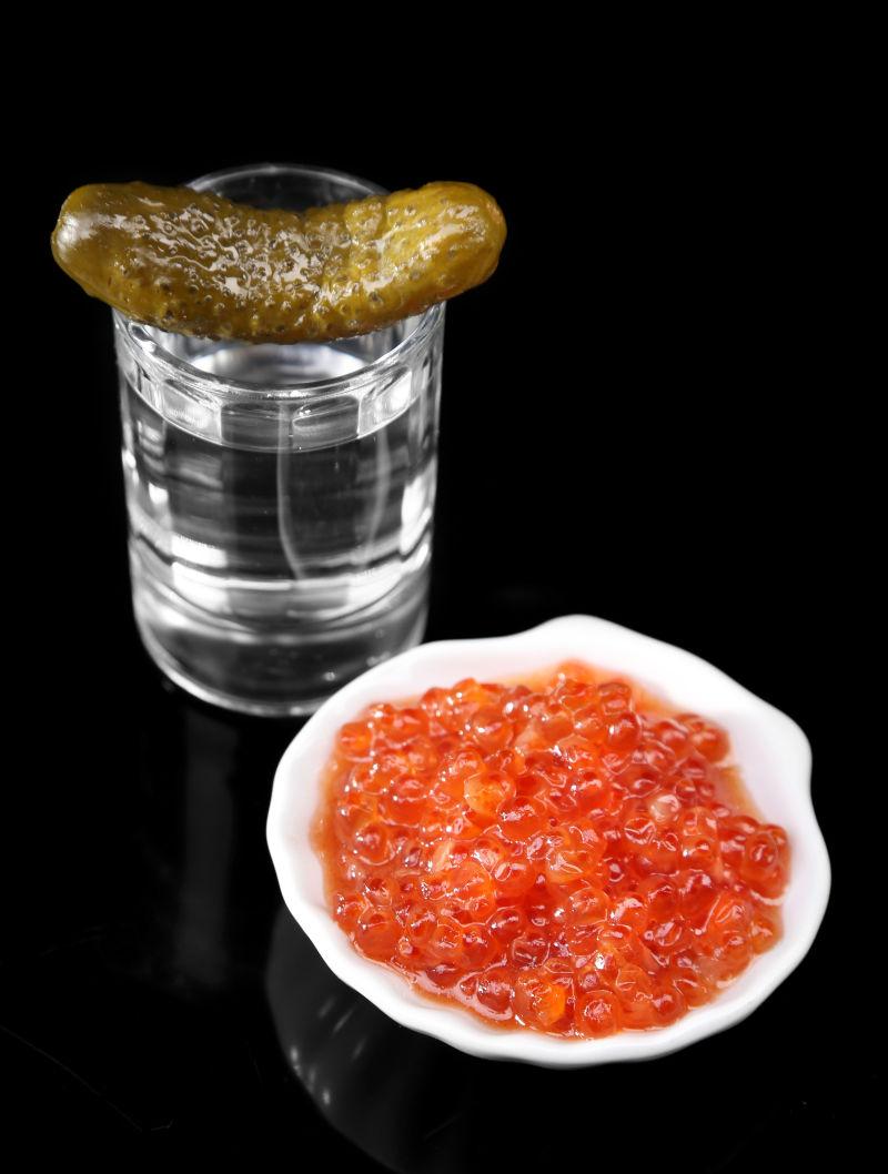 黑色背景下红鱼子酱和黄瓜子玻璃杯上