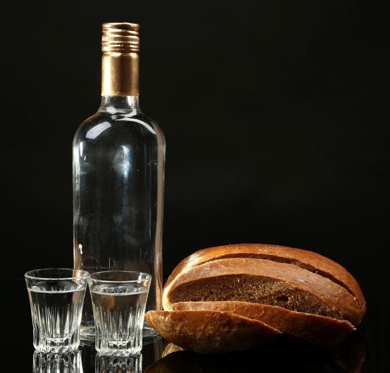 黑色背景下一瓶伏特加和新鲜面包与酒杯