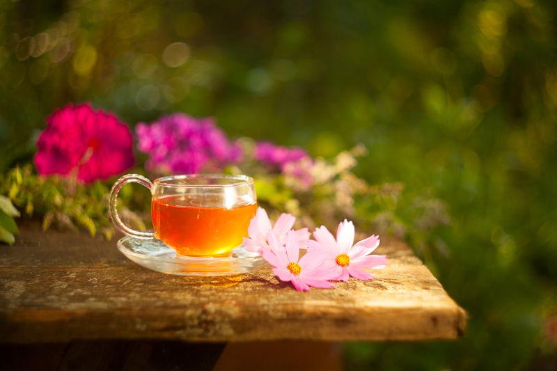 户外放在木桌上的花朵和一杯绿茶