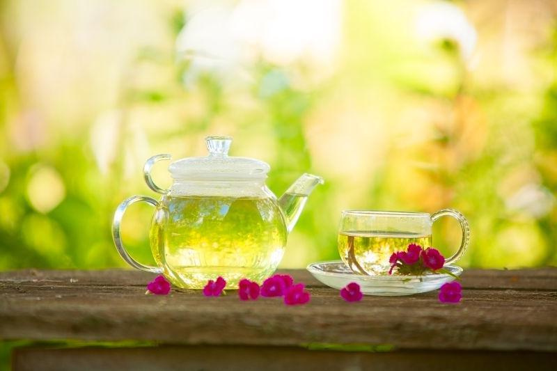 户外虚化背景下木桌上的玻璃茶具和里边的绿茶