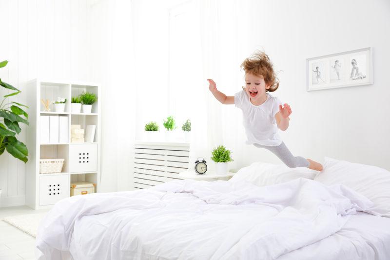 玩得开心的小女孩在床上蹦蹦跳跳