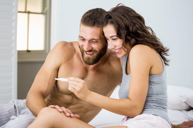 床上笑着脸看测孕结果的夫妻