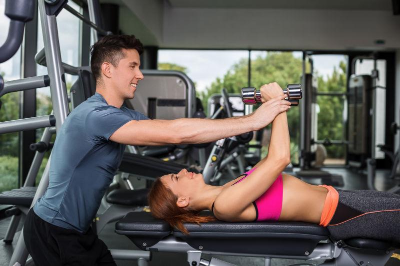 在健身教练的指导健身女孩练习哑铃