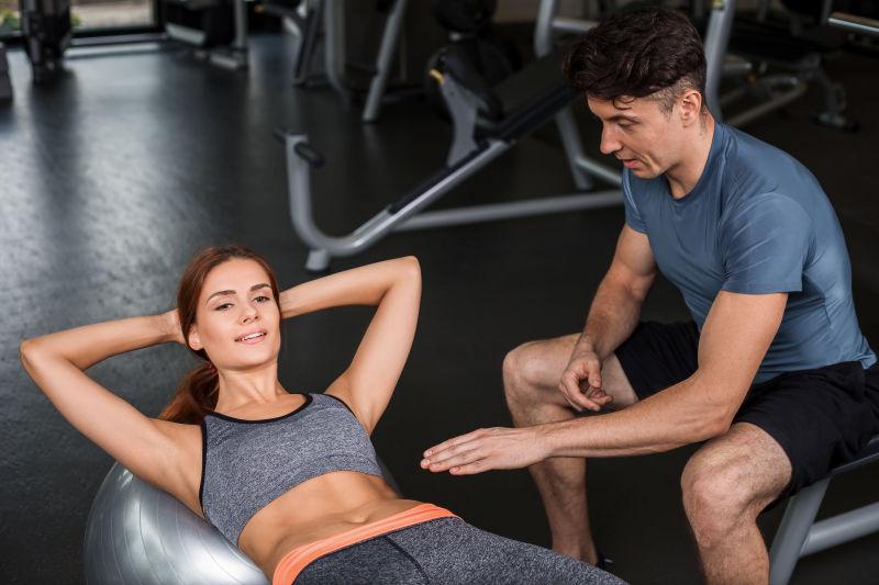 快乐的运动女孩在健身教练指导下做仰卧起坐