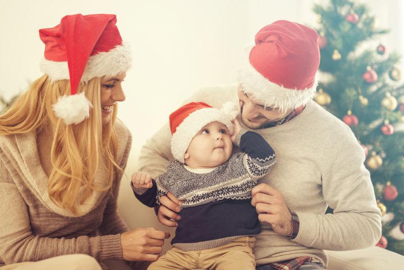 圣诞树边的带着圣诞帽的一家三口