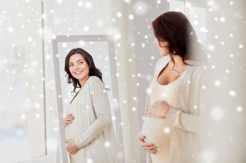 在冬天的家里对着雪镜的快乐的孕妇