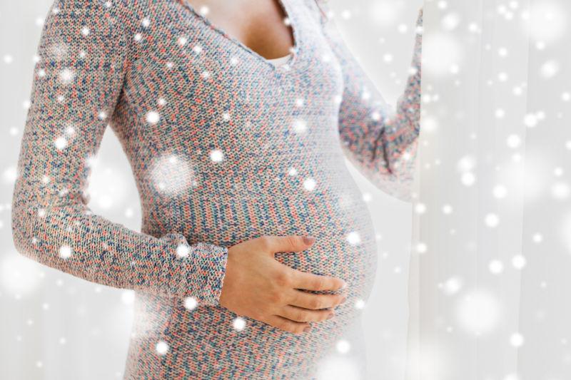 孕妇怀着大肚子望着窗外的雪