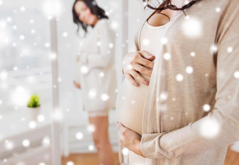 幸福的孕妇在家里对着雪照镜子