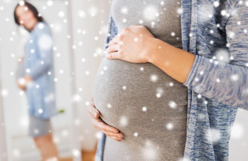 在圣诞节的家里对着雪镜的大肚子的快乐的孕妇