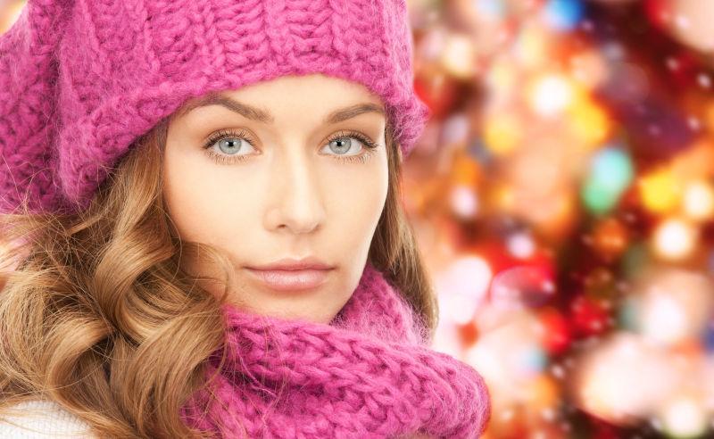 圣诞灯背景下的戴着红色帽子和围巾的年轻女子