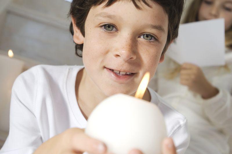 手上捧着白色蜡烛的小男孩