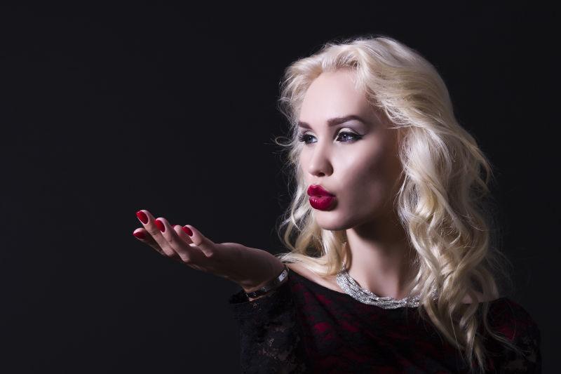 在黑色背景下的美丽的金发女人吹在他的手上