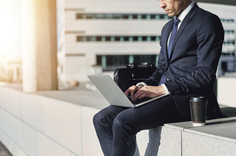 西装男做在户外用笔记本电脑打字