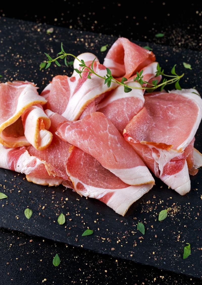 黑熏石板上新鲜的生熏腊肉片和中草药