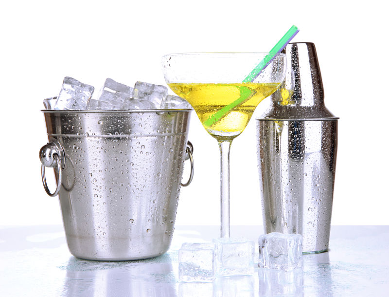 白色背景上装满冰块的金属冰桶旁放着鸡尾酒和摇酒壶