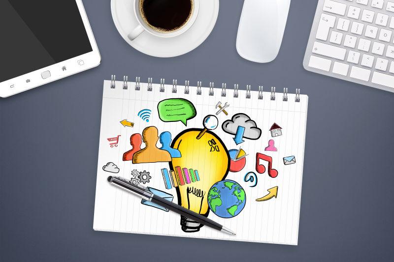 办公桌背景的笔记本上的手绘灯泡和多媒体图标