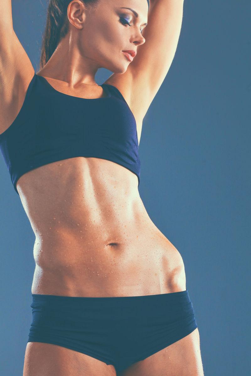 神蓝色背景下举起双臂站着的有着健美身材的美女