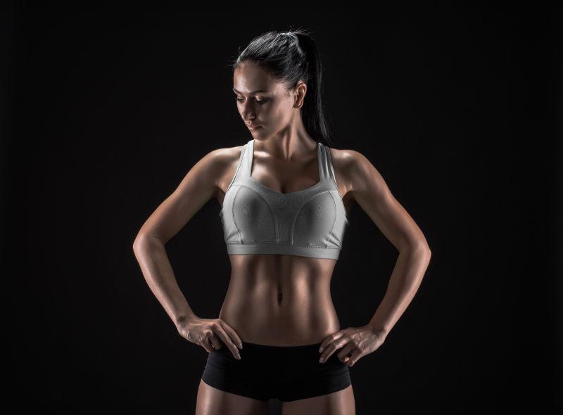 黑色背景下双手叉腰看下方的有着健美身材的美女