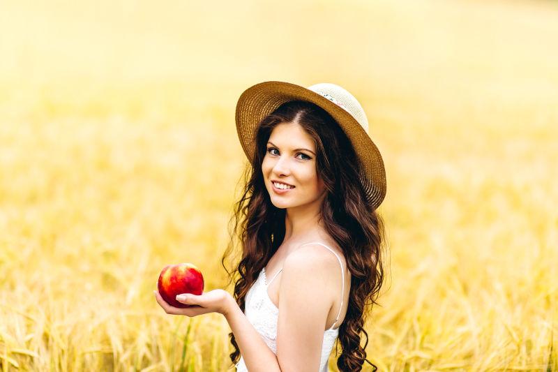 戴帽子的长发美女拿着苹果站在草地上