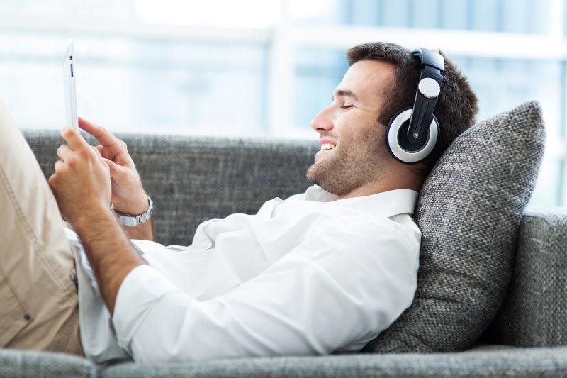 戴着耳机躺在沙发上使用平板的男人