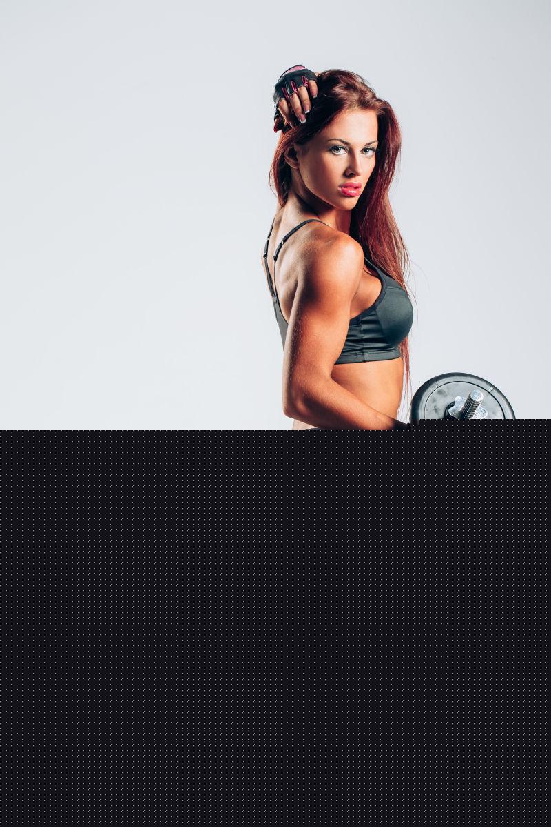 白色背景下穿着黑色套装拿着哑铃练习的有着健美身材的美女