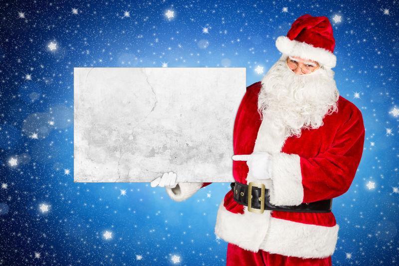 蓝色闪亮的星星夜空下的圣诞老人手里拿着的空广告牌