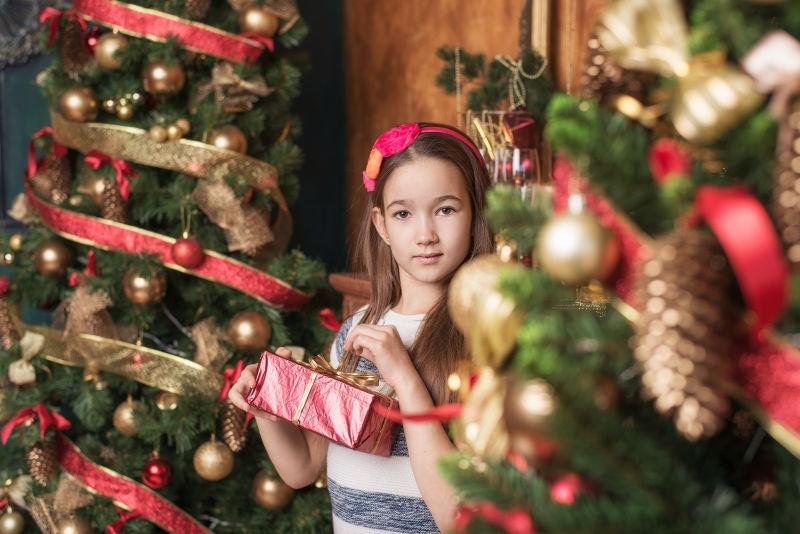 可爱的小女孩戴着红色头巾在圣诞树旁打开礼物