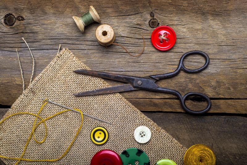 木桌背景下亚麻布上的剪刀纽扣和针线等缝纫工具