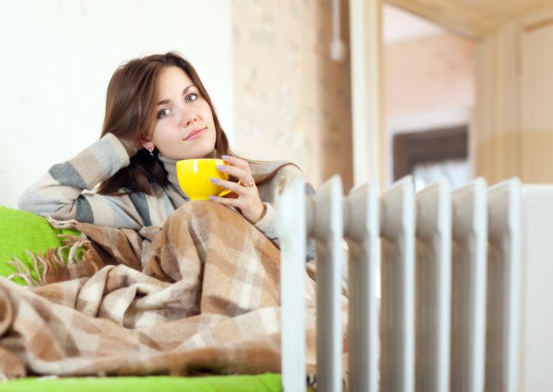 家用电暖器附近的女人捧着黄色茶杯