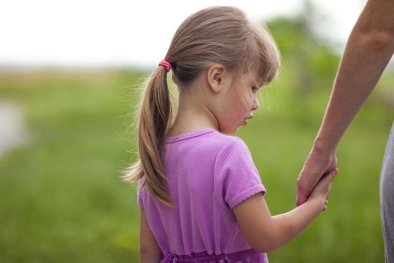 金发小女孩牵着妈妈的手在草地上