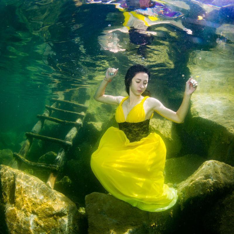 穿着黄色裙子的在水下楼梯旁的年轻优雅的女人