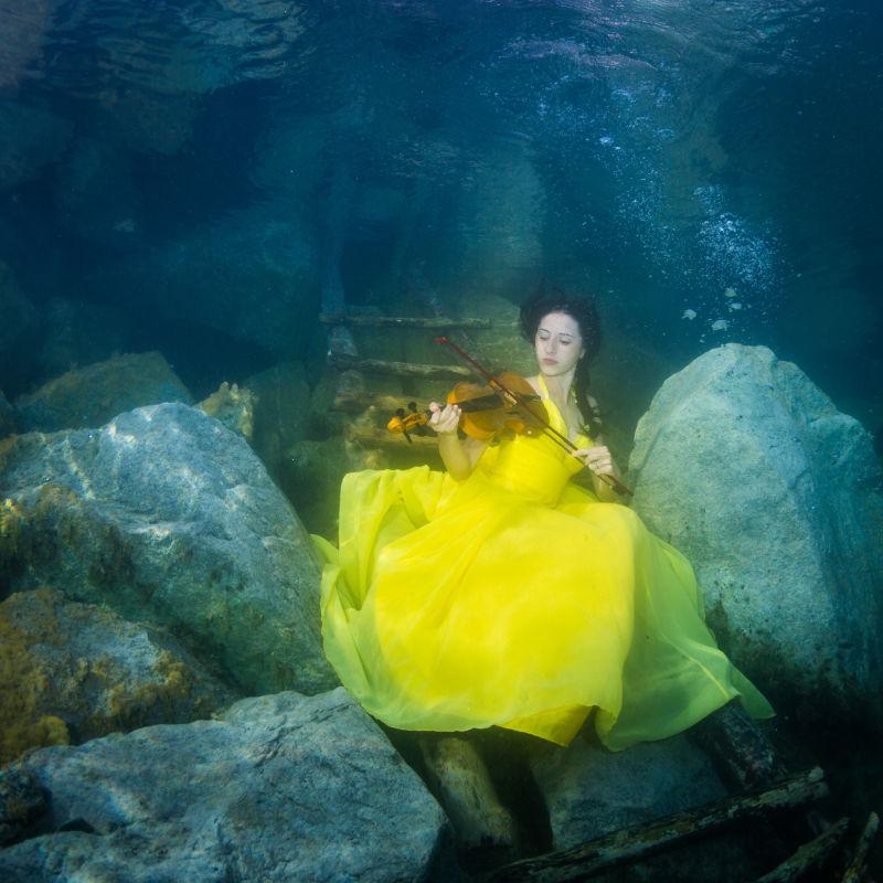 在水下楼梯上穿着裙子的年轻优雅的女子拉小提琴