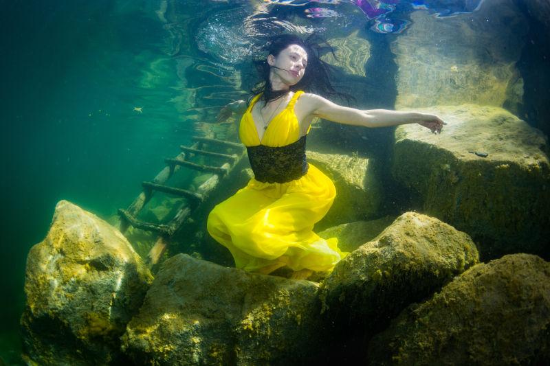 摆在水下楼梯旁的穿着一件裙子的年轻优雅的女孩