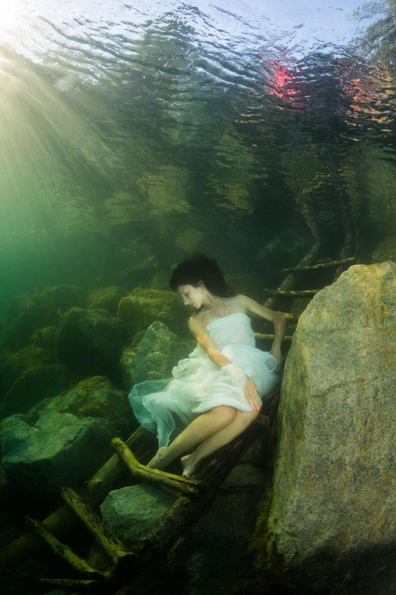 在水下楼梯上的穿着裙子的年轻的优雅女人
