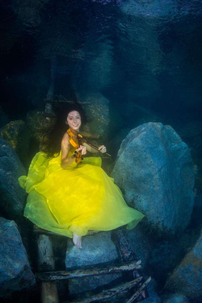 微笑着拉小提琴的年轻优雅的女人在水下楼梯上