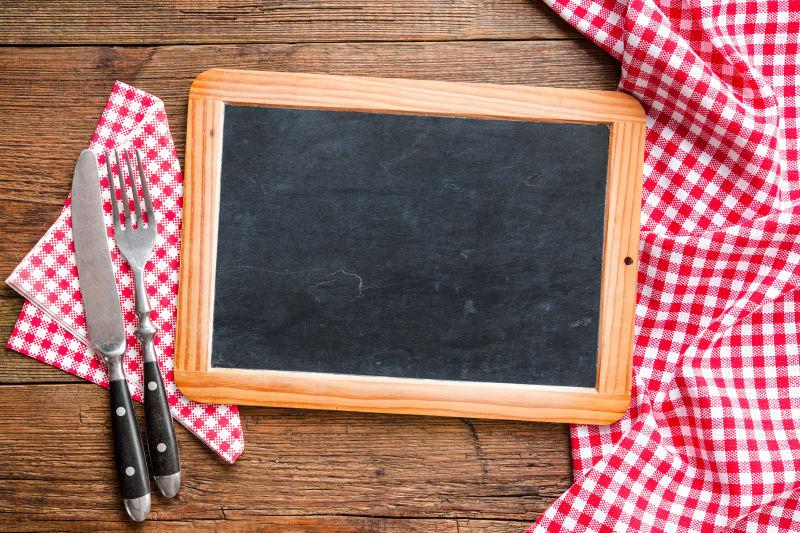 木质桌板上的黑板和红格子台布上的餐具