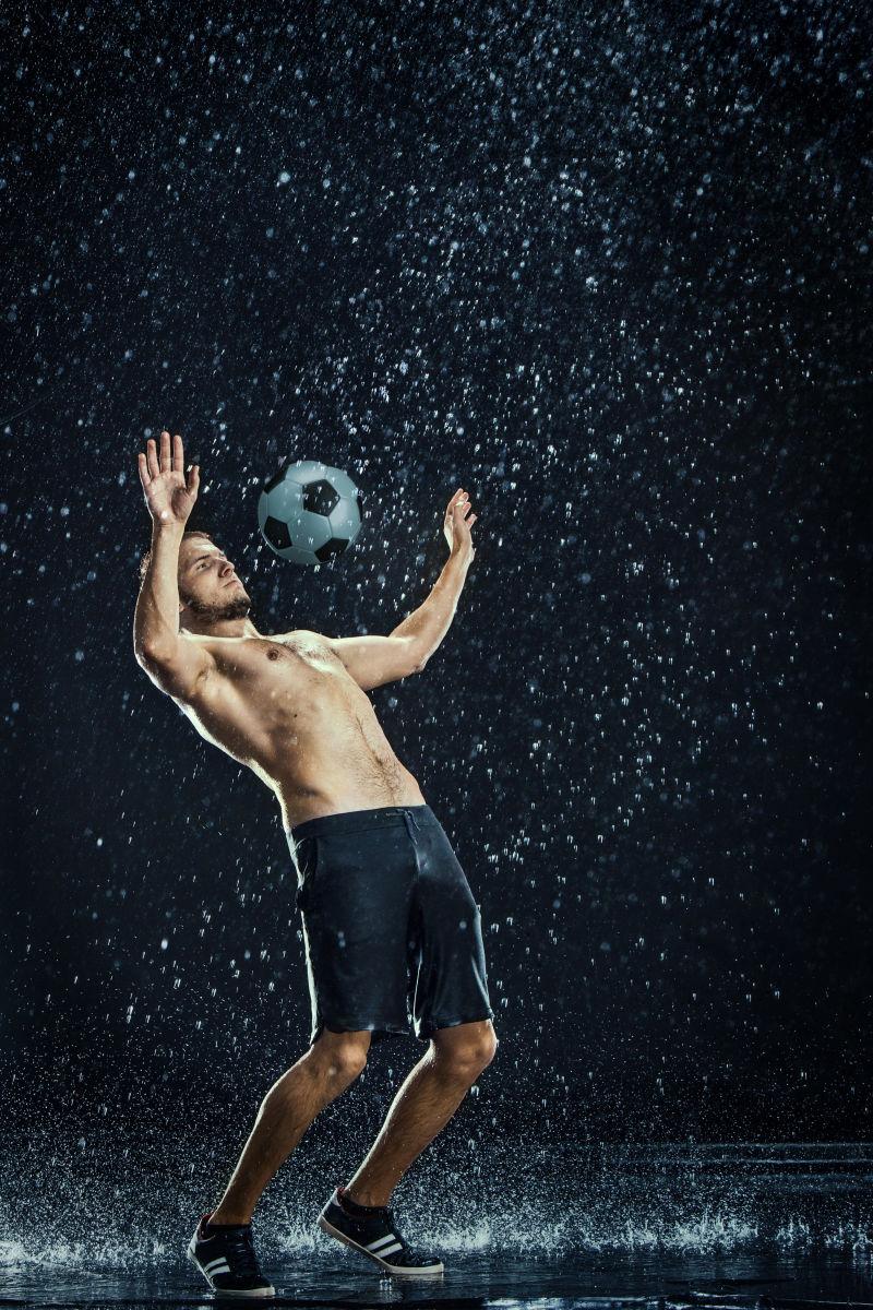 在黑色背景下玩足球的运动员和他周围的水滴