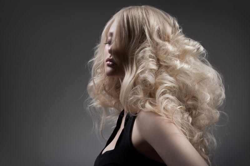 灰色背景前闭着眼的金色长卷发美女