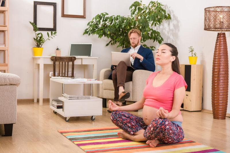 孕妇在家中做瑜伽和后面的丈夫