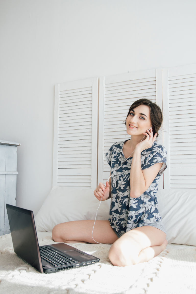 在床上用笔记本电脑听音乐的女人