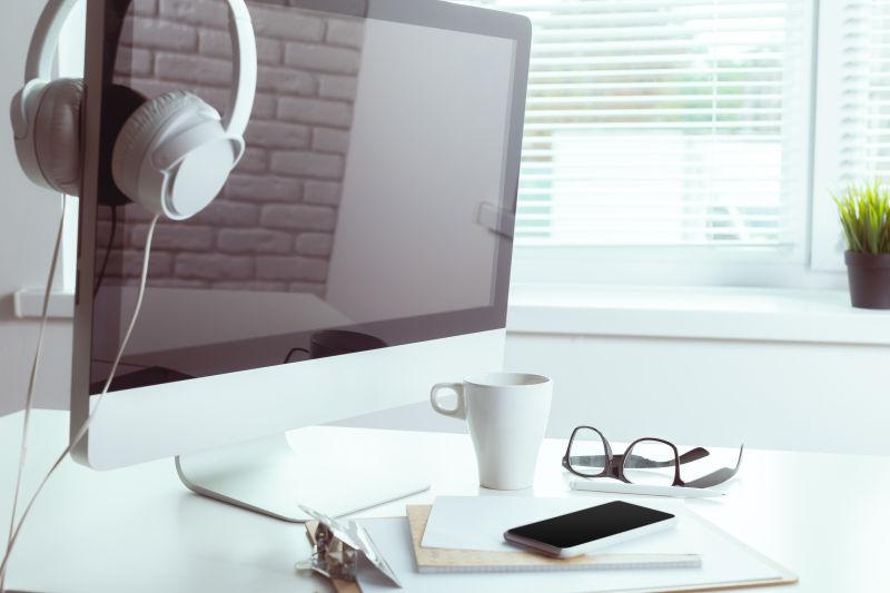 挂着耳机的电脑下面有个眼镜和手机还有一个咖啡杯子