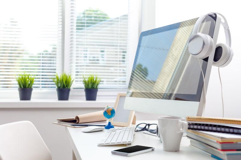 床上边的白色办公桌上有一台苹果电脑