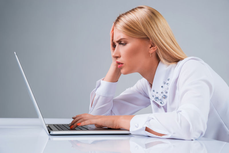 办公桌前用笔记本电脑工作的女人面露疲惫