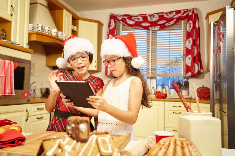 带着圣诞帽的一对姐妹在厨房浏览平板电脑