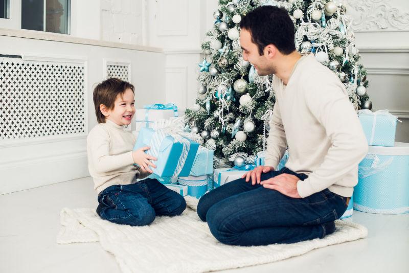 跪在圣诞树前拿着礼物的父子