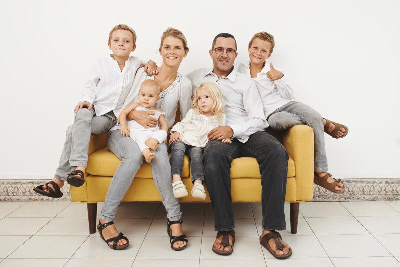 白色背景上坐在黄色沙发上穿着白色衣服的一家人