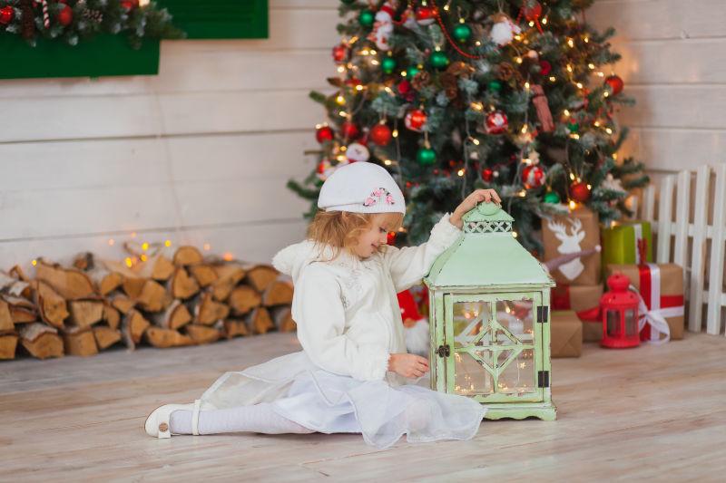 可是的小女孩坐在圣诞树旁拿着一只漂亮的灯笼