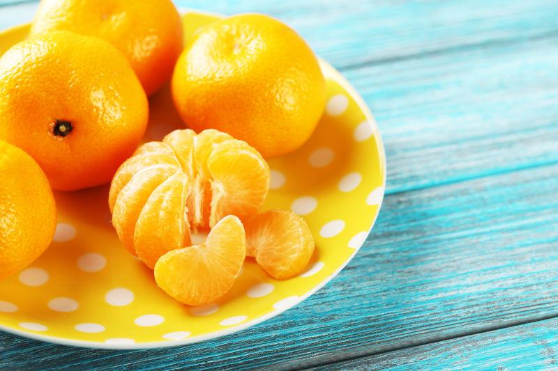 蓝色木桌上黄色盘子里的成熟的黄色橘子