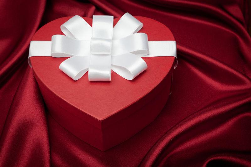 红色缎子背景下白色缎子蝴蝶结心形礼盒