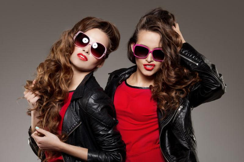灰色背景下两个带着太阳眼镜的时尚卷发美女